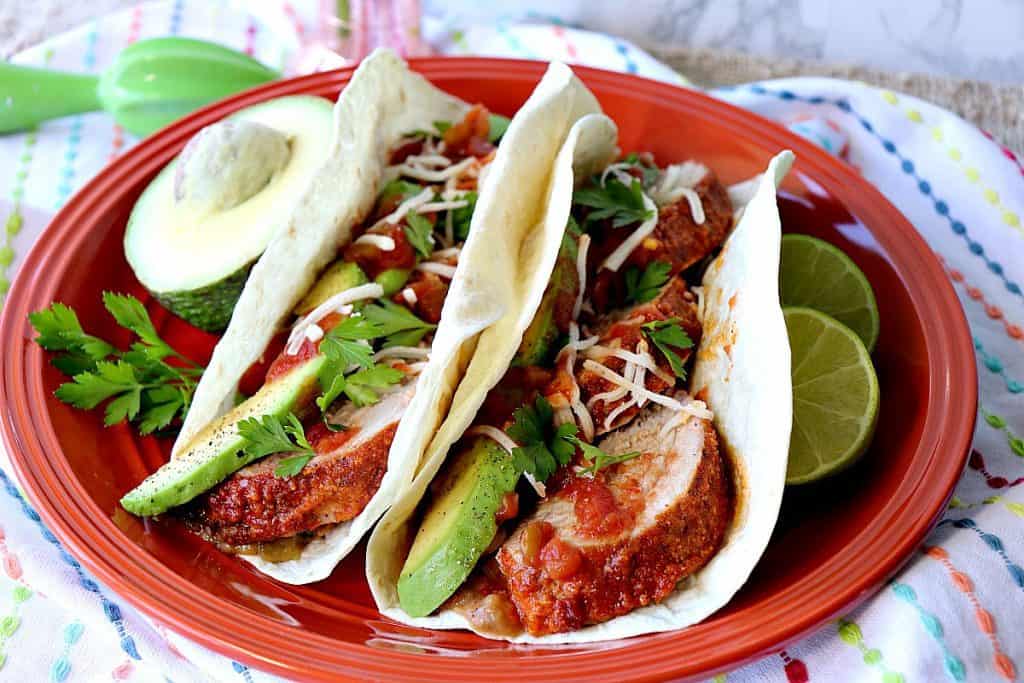 Two Mexican Pork Tenderloin Tacos on an orange plate with avocados and lime.