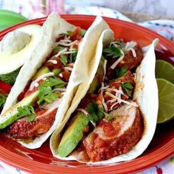 Two Mexican Pork Tenderloin Tacos on an orange plate with avocados and lime.