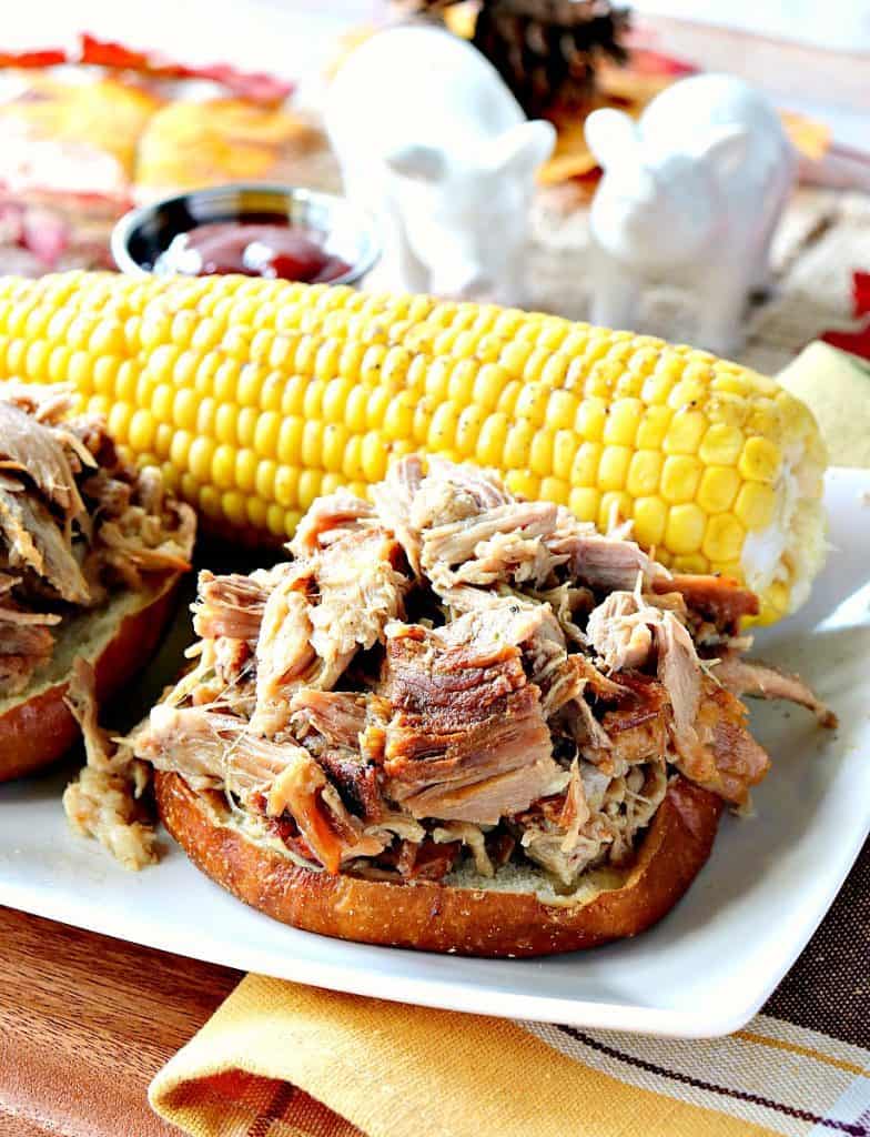 Closeup photo of an open faced pulled pork sandwich made in the slow cooker with a ear of corn in the background.