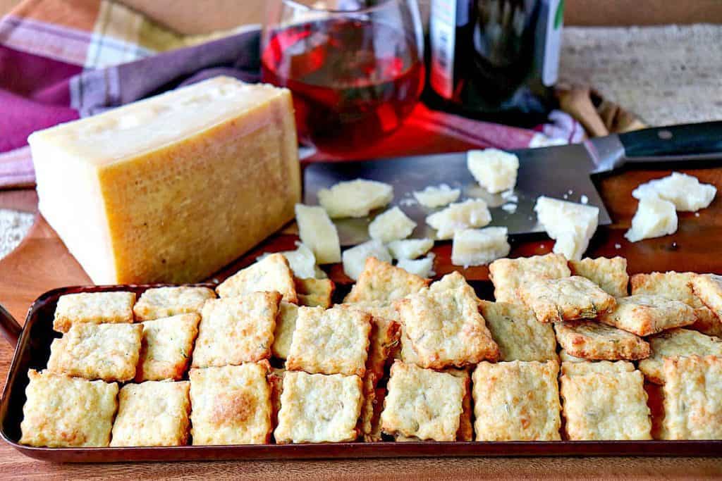 A horizontal photo of a tray of Parmesan fennel crackers with a wedge of Parmesan cheese in the background.