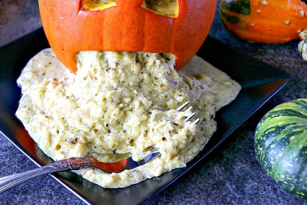 Horizontal overhead photo of a vomiting pumpkin with basil pesto spaghetti squash for Halloween on a black plate with a fork.