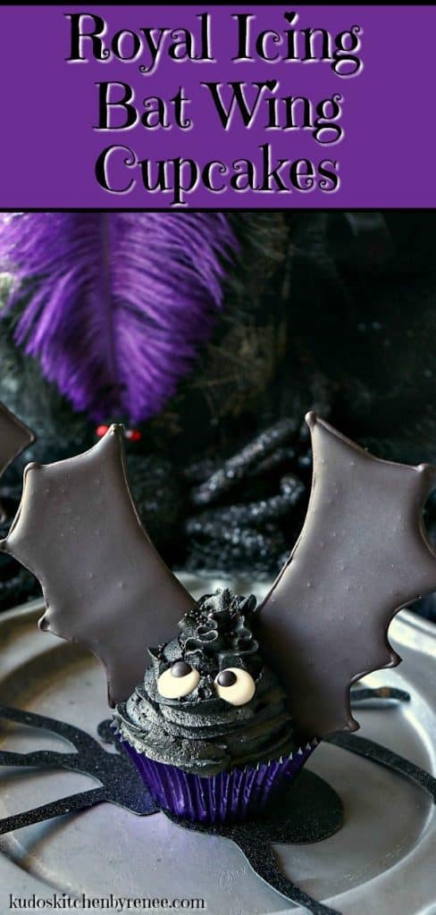  A closeup photo of a bat wing cupcake on a pewter plate with a purple feather and googly eyes.