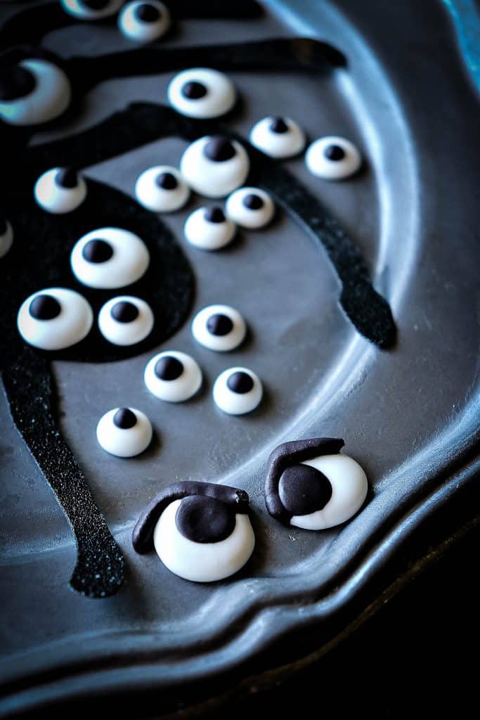 Closeup photo of a gray plate of Homemade Candy Eyeballs with a spider silhouette.