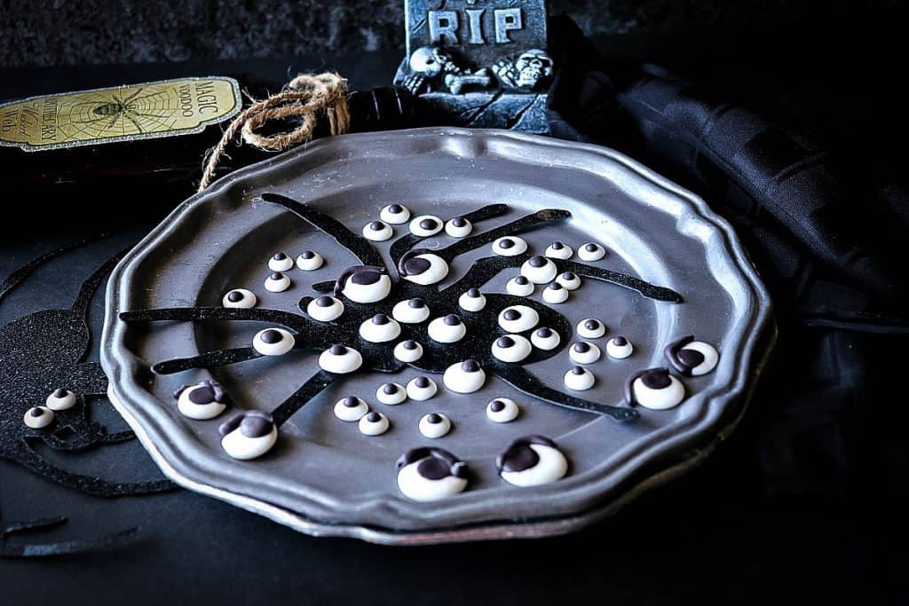 Spooky horizontal photo of a gray plate of Homemade Candy Eyeballs with a spider silhouette and black napkin.
