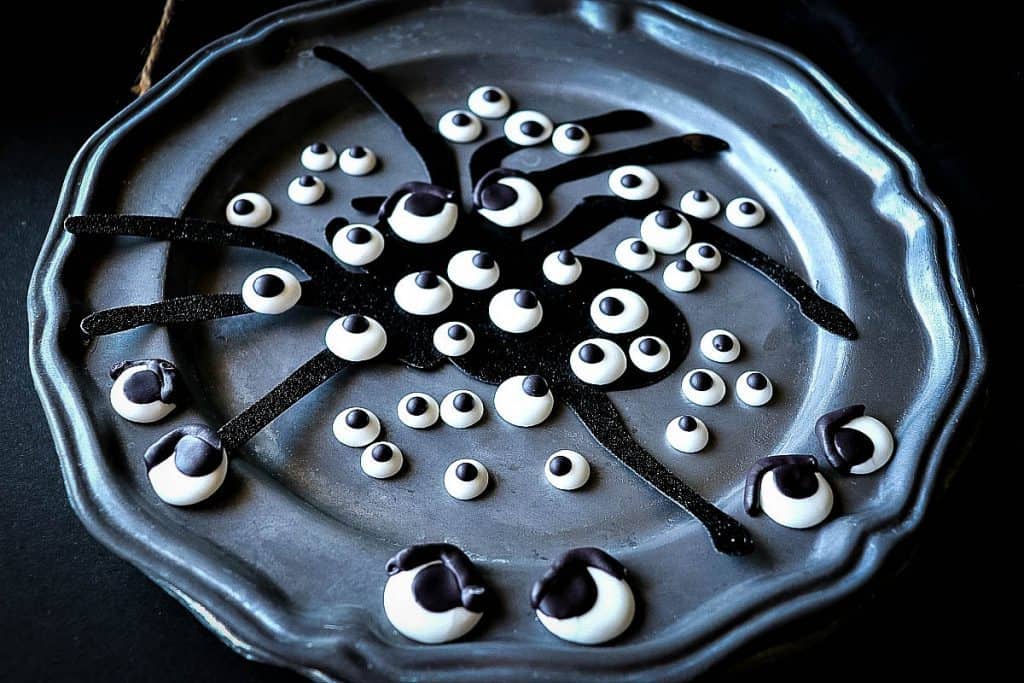 Horizontal overhead photo of a pewter plate with a spider silhouette and Homemade Candy Eyeballs.