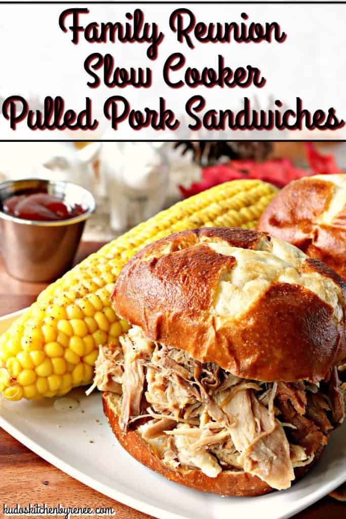 A closeup photo of a slow cooker pulled pork sandwich on a pretzel bun with a corn on the cob in the background and a cup BBQ sauce,