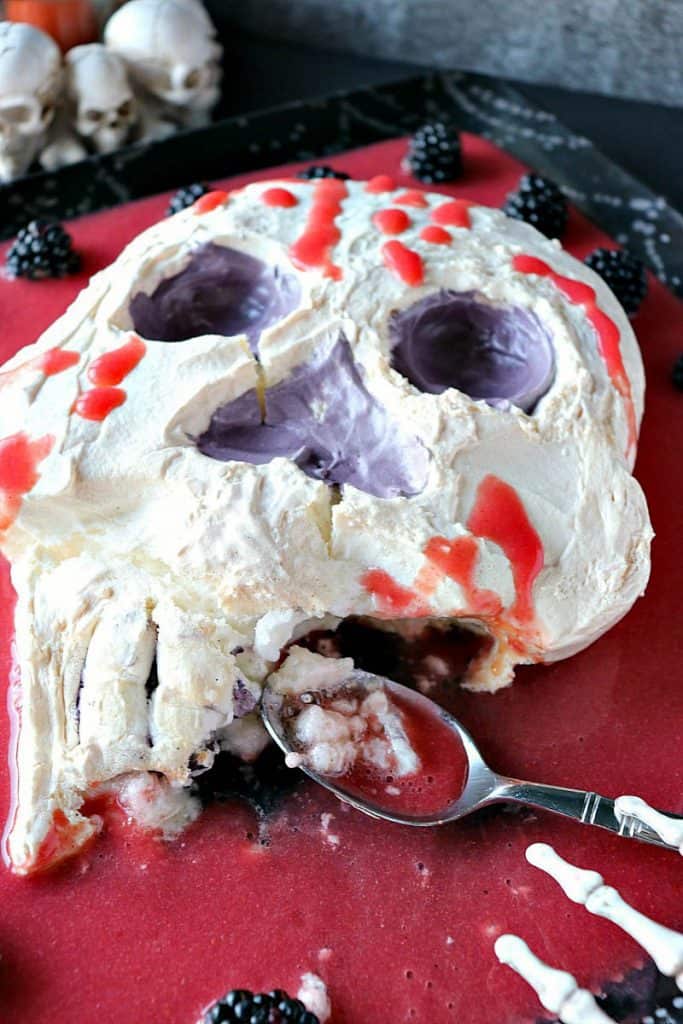 A vertical photo of a Swiss Meringue Skull with strawberry "blood" that's been partially eaten.