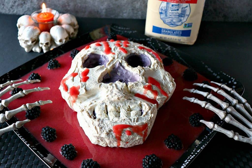 A Swiss Meringue Skull for Halloween along with a skull candle in the background and some blackberries on the platter.