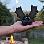 A hand holding a Batwing Cupcake with a moon and fire in the background.