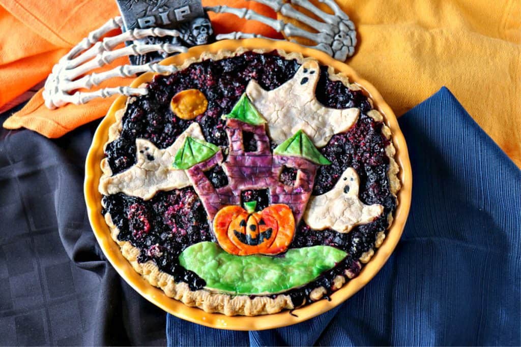 Overhead photo of a Halloween Pie with colorful napkins, ghosts, pumpkins, and skeleton hands.