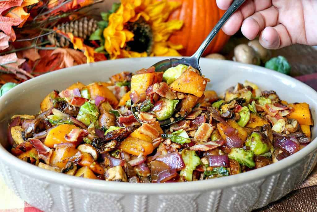 A hand holding a serving spoon of colorful sauteed autumn vegetables.