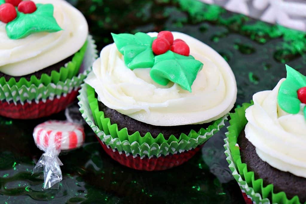 Three Holly Berry Cupcakes with Peppermint Buttercream Frosting on a plate with a peppermint candy on the side.