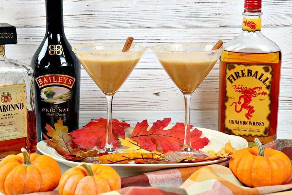 Two pumpkin spice martinis on a tray with pumpkins and leaves