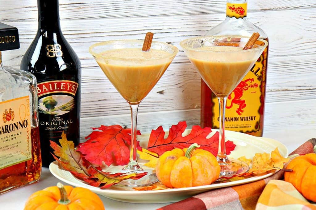 Two martini glasses filled with pumpkin spice martinis and autumn leaves on a platter