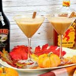 Two martini glasses filled with pumpkin spice martinis and autumn leaves on a platter