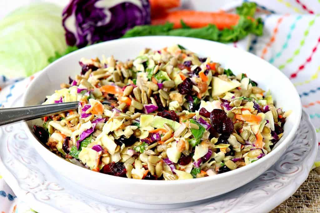 Colorful coleslaw in a white bowl with a spoon and a colorful napkin in the background.