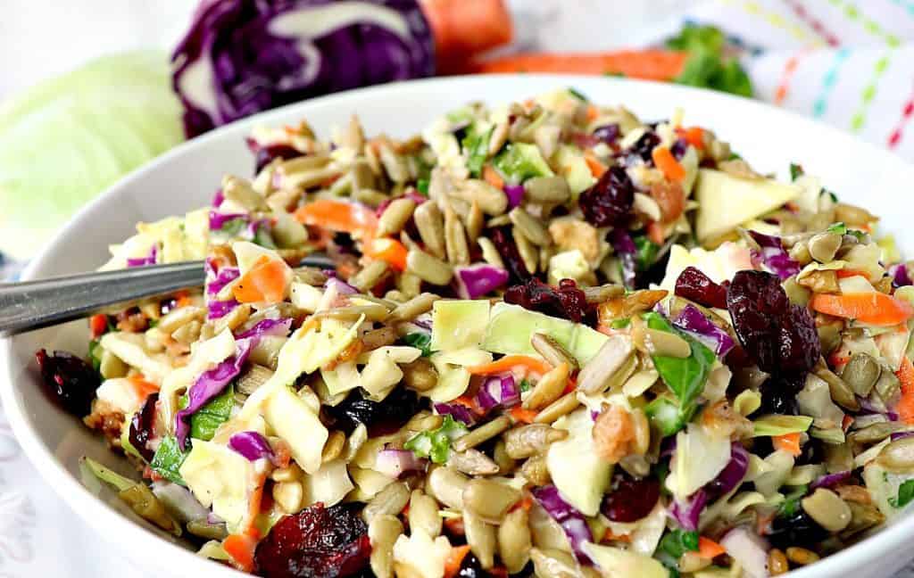 A horizontal photo of a bowl of sunflower crunch chopped salad in a white bowl with a spoon.