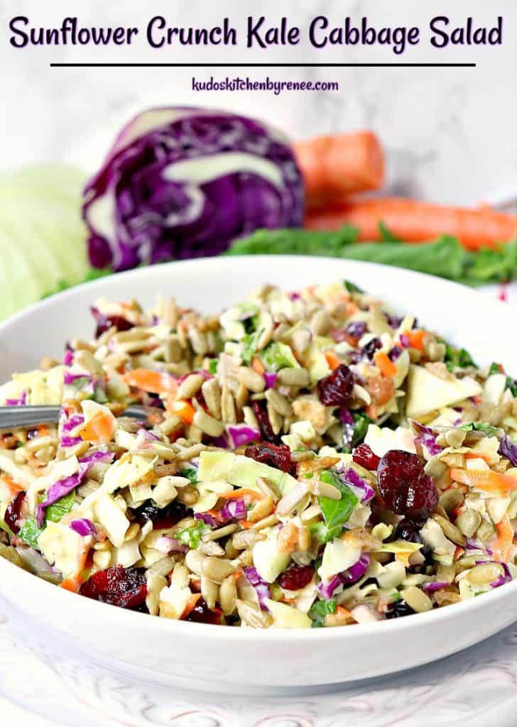 Colorful bowl of kale cabbage salad with purple cabbage and carrots in the background.