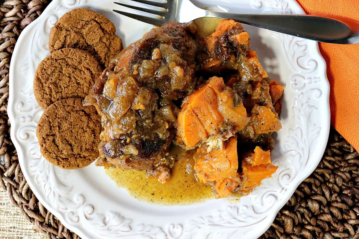 A white plate filled with tender sweet potatoes, braised apple cider chicken breast, and 3 gingersnap cookies.