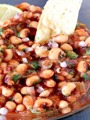 An offset bowl of Black-Eyed Pea Salsa with lime wedges and cilantro.