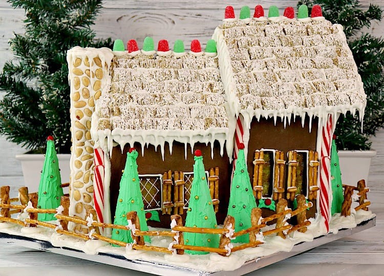 This Gingerbread House Tutorial is a comprehensive recipe along with tips and tricks so you can learn from our successes, as well as our mistakes. - kudoskitchenbyrenee.com Back of a decorated gingerbread house with snow, candy, icicles, and in a snowy yard with a fence. - kudoskitchenbyrenee.com
