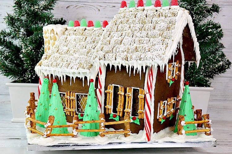Decorated gingerbread house with candy windows, pretzel shutters, snow covered yard, mini wheat roof, and gumdrop accents. - kudoskitchenbyrenee.com