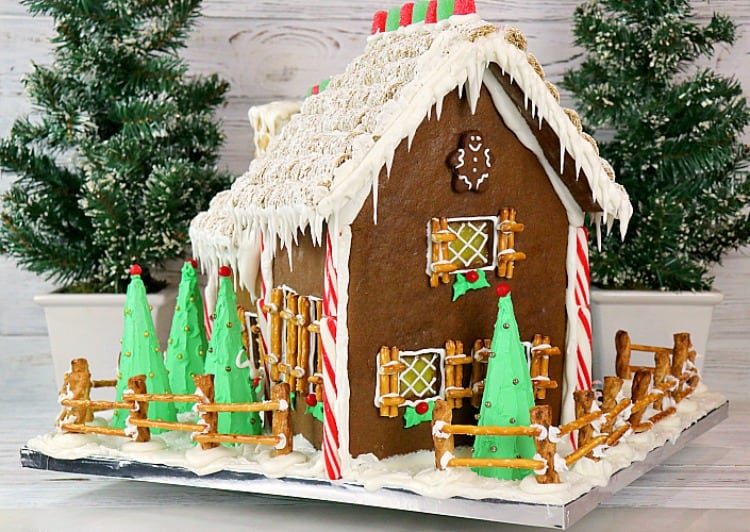 Side view of decorated gingerbread house with candy canes, gum drops, icicles, pretzel shutters, and mini wheat roof. - kudoskitchenbyrenee.com