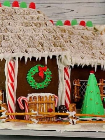 A cute decorated Gingerbread House Recipe and Tutorial using peppermint sticks, royal icing, pretzels, and gum drops.