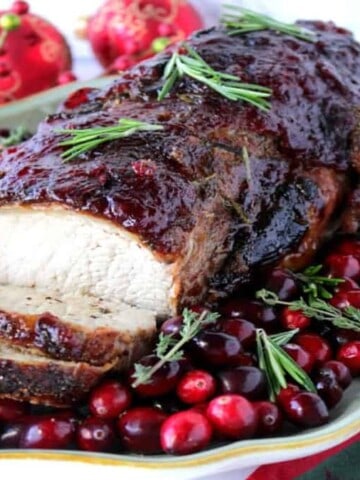 A sliced Pork Roast with Cranberry Relish on a platter with fresh herb and fresh cranberry garnish.