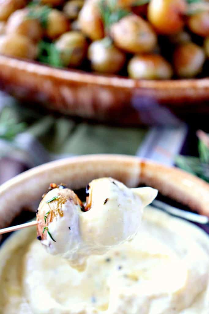 Closeup photo of two roasted baby potatoes on a wooden pick that have been dipped into creamy sauce.