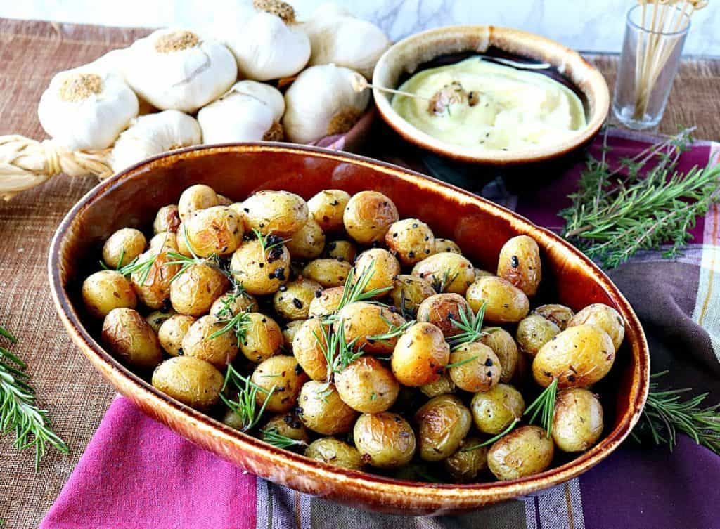 Overhead photo of a large brown oval bowl filled with roasted baby potatoes with fresh herbs and garlic.