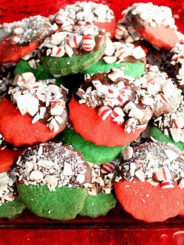 A bunch of red and green Peppermint Shortbread Cookies dipped in chocolate and peppermint on a red plate.