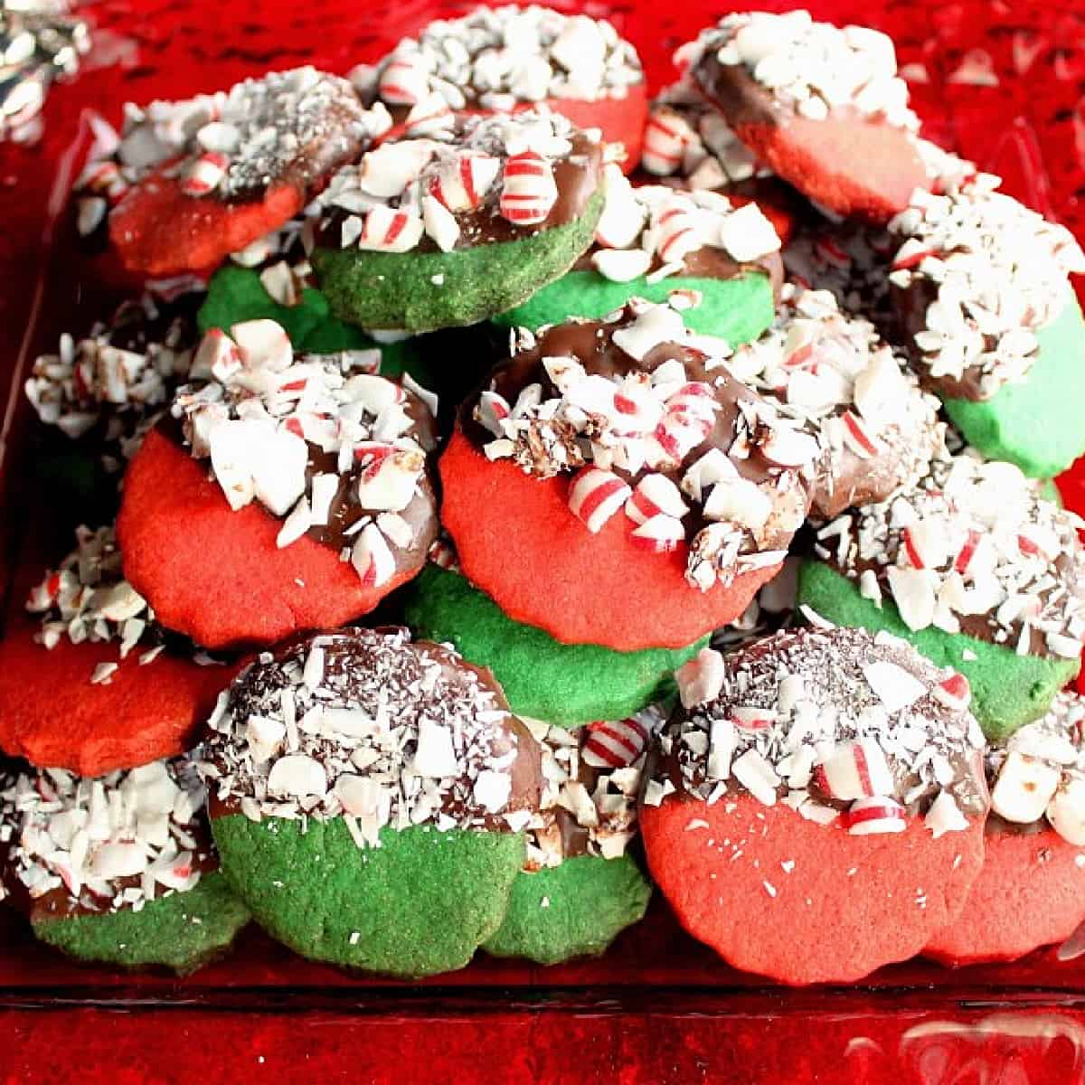 A bunch of red and green Peppermint Shortbread Cookies dipped in chocolate and peppermint on a red plate.