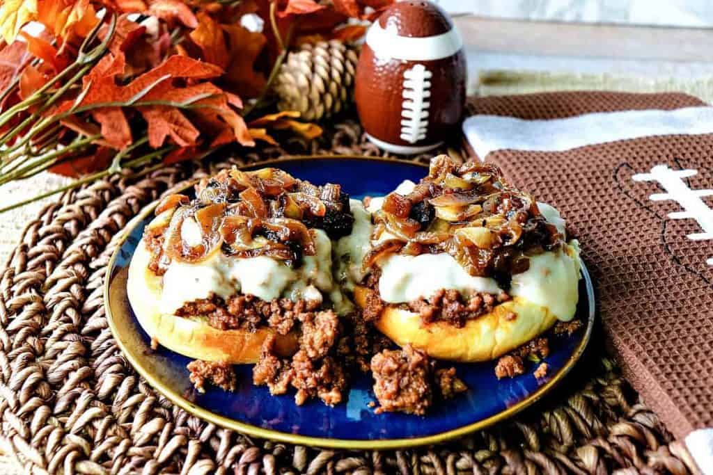 A open face sandwich of French Onion Sloppy Joes on a blue plate with melted cheese and caramelized onions.