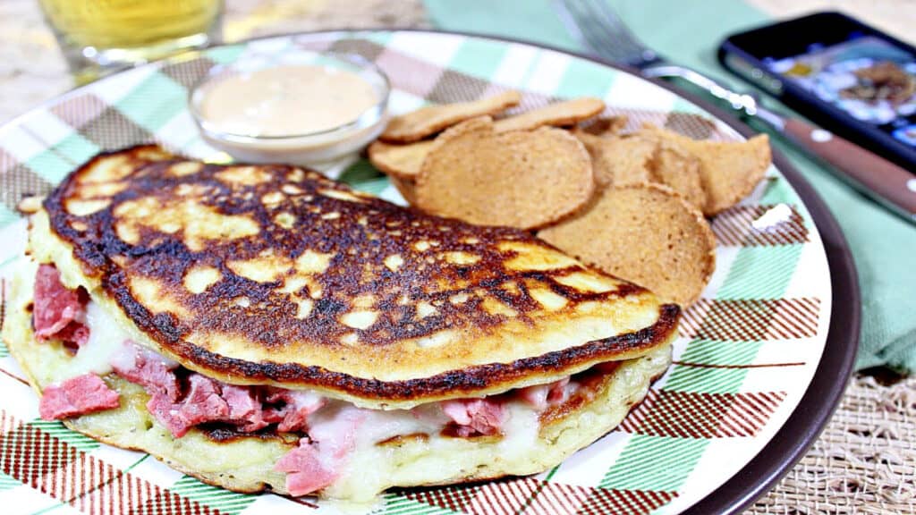 An Irish Corned Beef Boxty on a brown and green plaid plate with chips on the side.