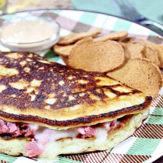 An Irish Corned Beef Boxty on a brown and green plaid plate with chips on the side.