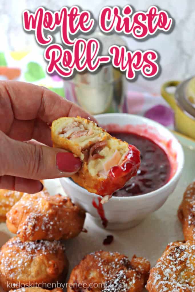 A hand holding a fried monte cristo appetizer roll-up dipped in raspberry jam