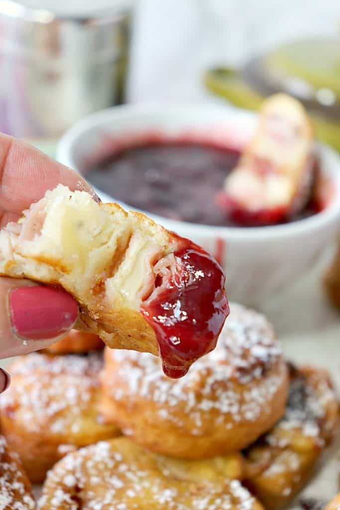 Vertical Closeup bite of Monte Cristo Tortilla Roll Ups dipped in Raspberry Sauce 