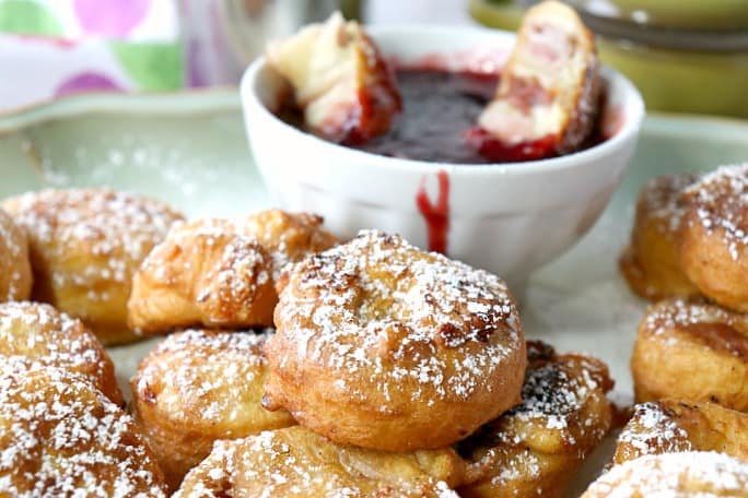 A platter of Monte Cristo appetizer roll-up along with a bowl of raspberry jam.