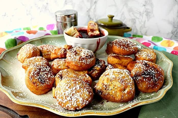 A full platter of Monte Cristo appetizer roll-up sprinkled with powdered sugar and a multi-colored polka dot napkin the the background.