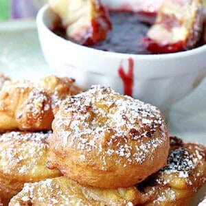 A Monte Cristo Appetizers covered in powdered sugar with some raspberry sauce in the background.