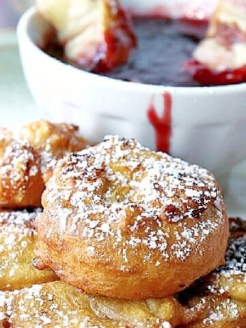 A Monte Cristo Appetizers covered in powdered sugar with some raspberry sauce in the background.