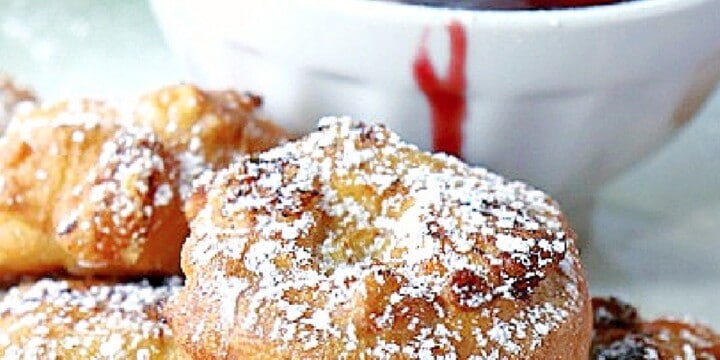 A Monte Cristo Appetizers covered in powdered sugar with some raspberry sauce in the background.