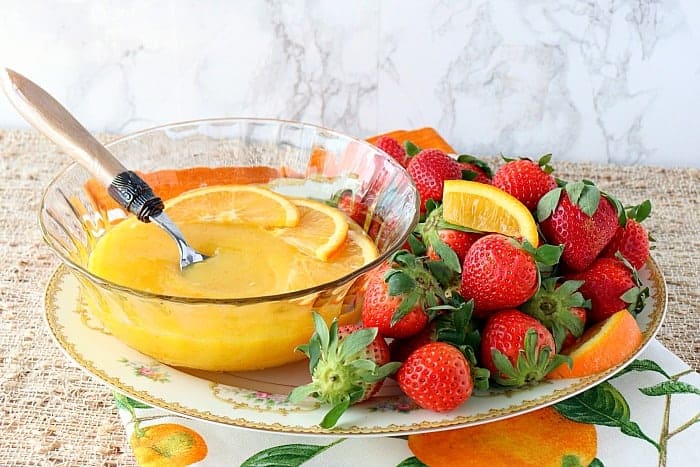 A glass bowl of homemade orange curd on a platter with strawberries.