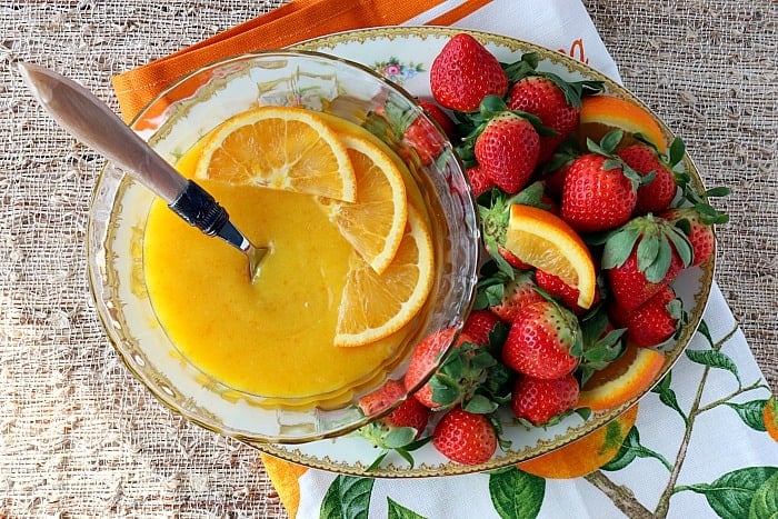 Overheat picture of a bowl of homemade orange curd on a plate with fresh strawberries.