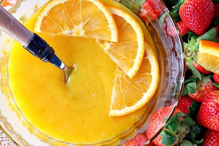 Closeup picture of homemade orange curd with three slices of fresh orange and a spoon.