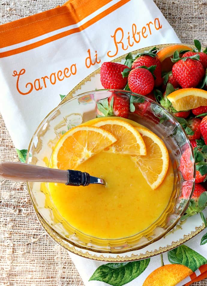 Overhead vertical image of a bowl of homemade orange curd with strawberries and orange slices.