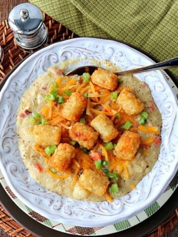 A white bowl filled with Tater Tot Chowder with a spoon.