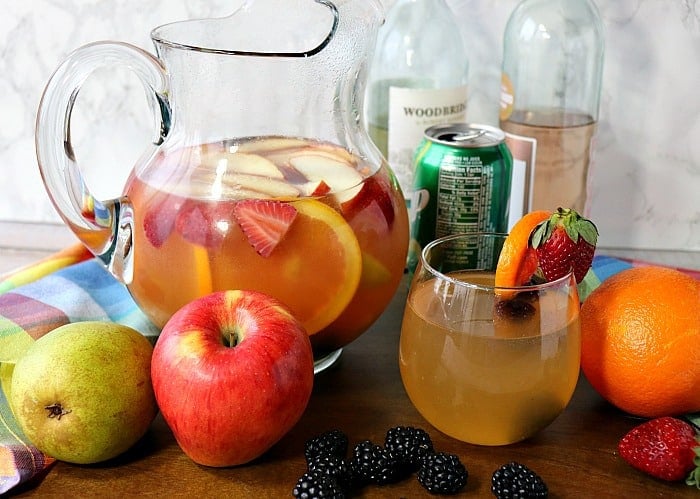 A pitcher filled with blackberry sangria with apples pears, strawberries and a glass.