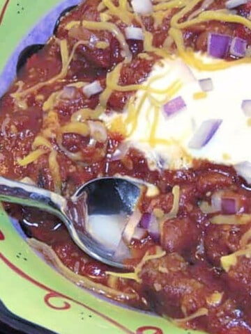 A green bowl filled with Smoky Beer Chili along with a spoon and a dollop of sour cream.